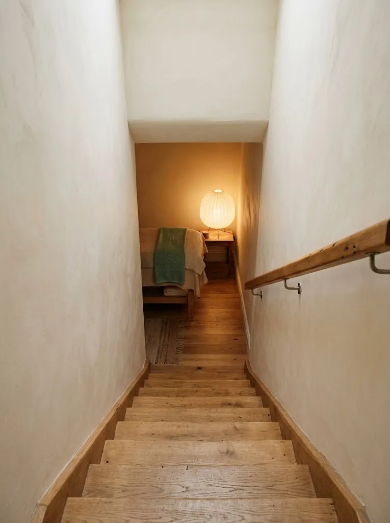 Uma escada estreita de degraus de madeira quente a descer para uma sala de luz suave